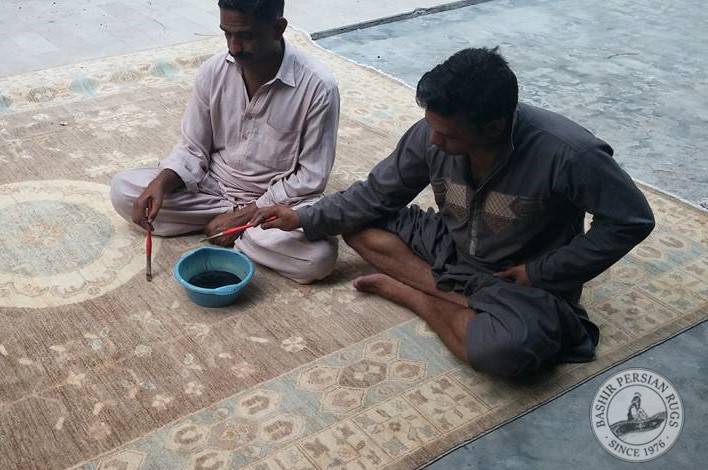 Pakistani rug artisans using their paint brushes to  perform some minor color touch ups with vegetable dyes on a hand-knotted Oushak style rug.